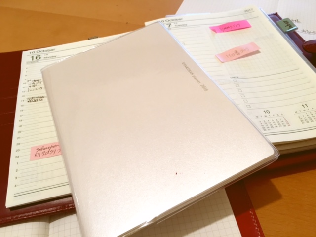2018年の逆算手帳き表紙です。後ろにみえるのは、あな吉手帳を自分流にアレンジした、1日1頁の手帳です。これは持ち歩けないのが難点。いつも机の上に乗りっばなしです。